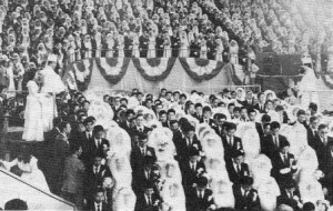 １９８２年１０月、ソウルにおける５８３７組のカップルの祝福。文夫妻は白い式服を着て、カップルが列を成して通り過ぎるとき、彼らに聖水を振りまく。（２章66ページ下）